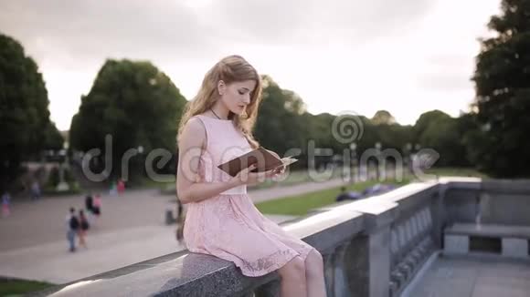 女孩坐在公园的岩石上看书用手纠正长发视频的预览图