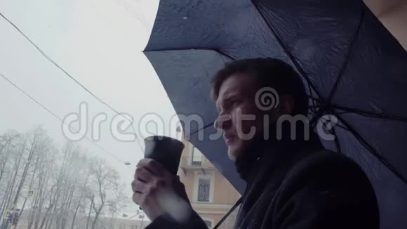 带着雨伞的年轻人站在雪地里喝着塑料杯里的咖啡视频的预览图