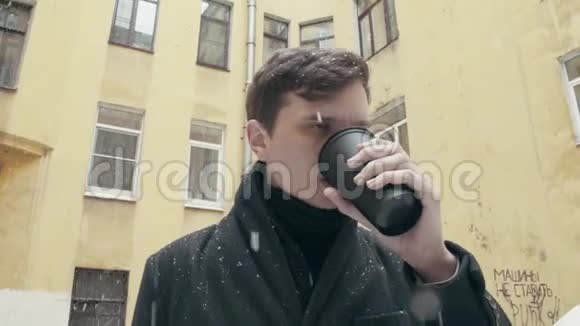 穿着外套的年轻人站在雪地里喝着黑色塑料杯里的咖啡视频的预览图
