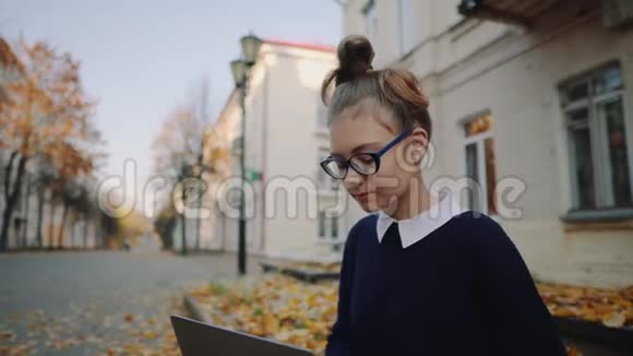 在秋城街的人行道上坐着一个漂亮的时髦少女用手提电脑女生视频的预览图