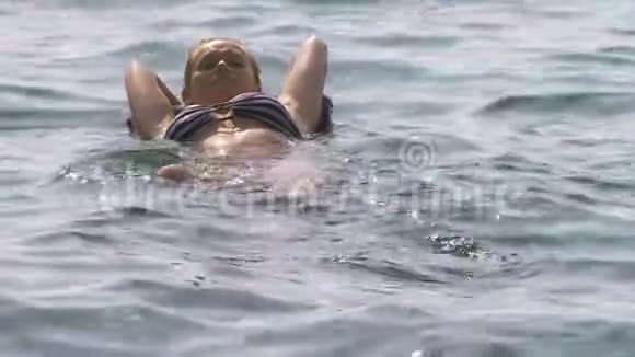 一个没有化妆的女人休息一个女孩躺在充气枕头上漂浮在海里4K慢动作视频的预览图