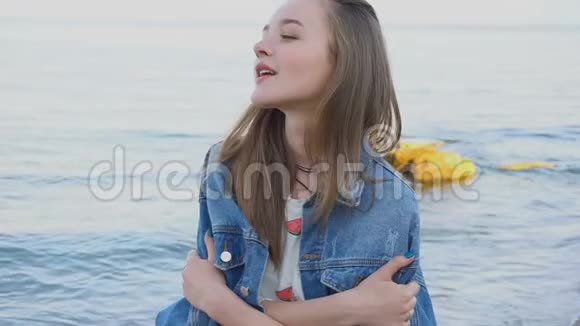 慢动作肖像可爱的女孩摆姿势和微笑的相机站在海边温暖的夏天晚上视频的预览图