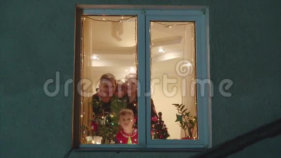 幸福的一家人透过窗户望着雪挥手致意视频的预览图