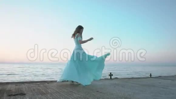 穿着一件蓝色长裙在海边享受生活的令人惊叹的黑发女郎视频的预览图