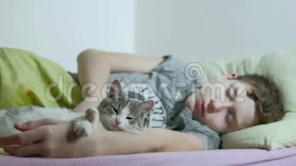 十几岁的男孩睡在床上一个在室内睡觉养宠物猫的疲惫的少年视频的预览图