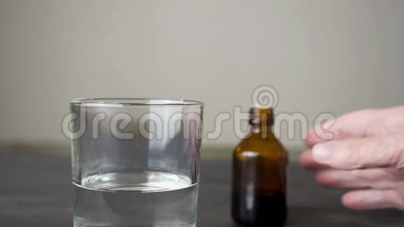 老年妇女用液体药物将药物滴入深色瓶子中的一杯水中视频的预览图