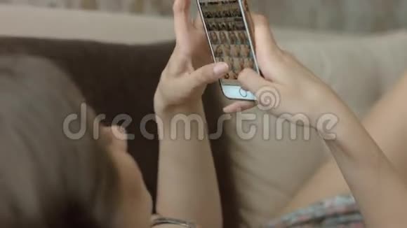 穿着睡衣的漂亮女人躺在沙发上看着手机上的照片视频的预览图