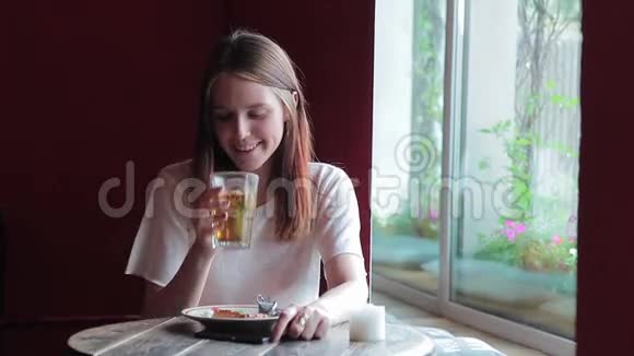 年轻女子喝茶看电话的肖像视频的预览图