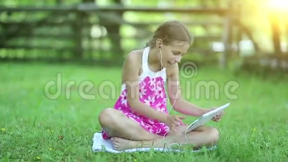 日落时分一个带着平板电脑的漂亮女孩坐在花园的草地上视频的预览图
