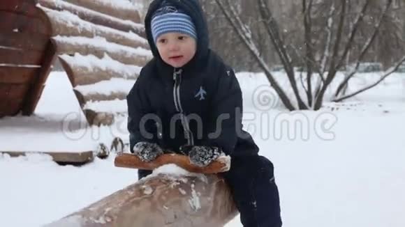 冬天的公园里下雪的时候小可爱的男孩在木跷跷板上视频的预览图