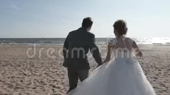 两个人手牵着手在海滩上奔跑背光镜头移动视频的预览图