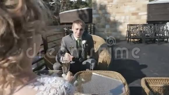 新郎新娘端着香槟酒杯坐在夏日咖啡馆的阳台上视频的预览图