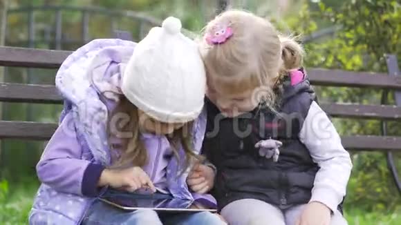 两个拿着平板电脑的小女孩坐在花园的长凳上视频的预览图