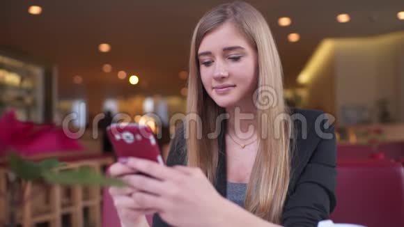 穿着黑色夹克的金发美女坐在咖啡馆A商店里她正在给她发短信视频的预览图