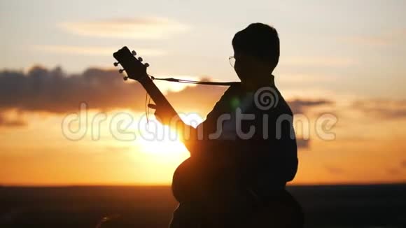 戴着圆眼镜的男孩在日落时分的田野里弹吉他视频的预览图