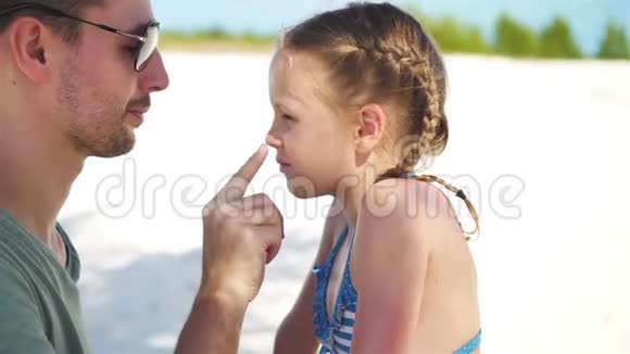 父母用防晒霜涂在孩子鼻子上阳光下可爱女孩的肖像视频的预览图
