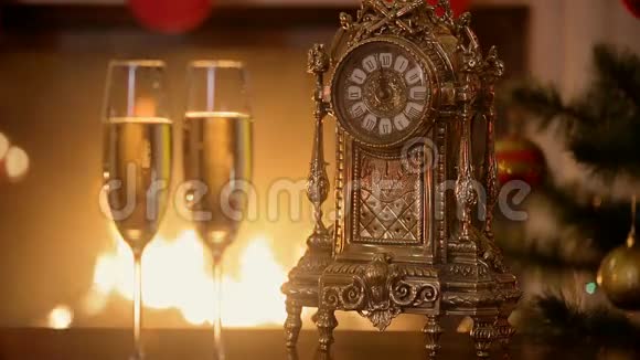 在燃烧的壁炉旁的桌子上在数着几分钟到新年的旧钟旁边特写两杯香槟视频的预览图