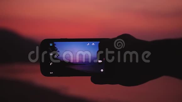 特写男手拿着手机在沙滩上拍一张美丽的日落照片慢动作1920x1080视频的预览图