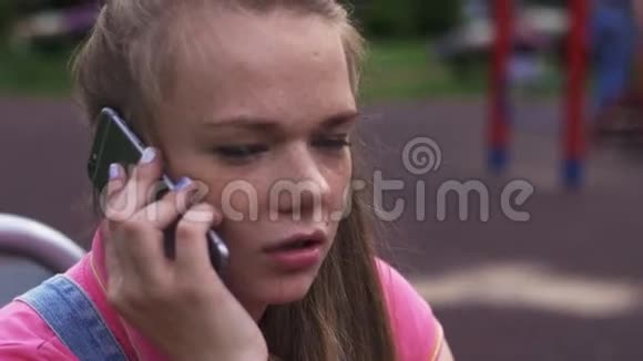 有雀斑的年轻漂亮女孩在操场上和电话交谈夏日公园视频的预览图