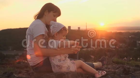 在夏天的傍晚妈妈和女儿坐在山上打电话视频的预览图