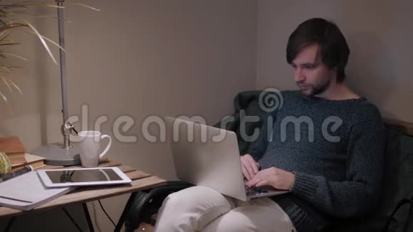 年轻的男性自由职业者在自然美食咖啡馆里坐在打开的笔记本电脑前一边用手机聊天视频的预览图