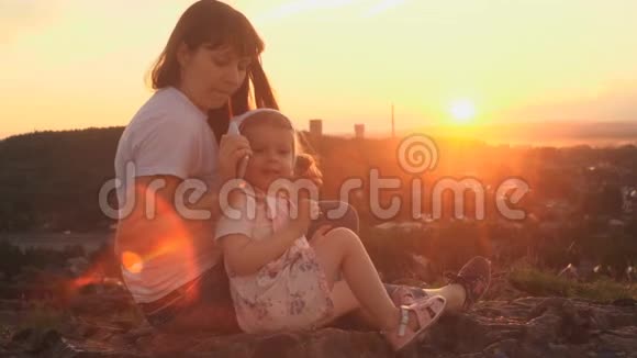 在夏天的傍晚妈妈和女儿坐在山上打电话视频的预览图