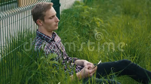 年轻人拿着手机坐在草地上视频的预览图