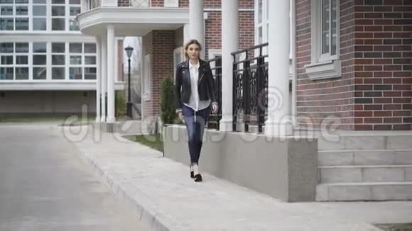 美丽的金发女郎自信的步态走在街上黑色皮夹克视频的预览图
