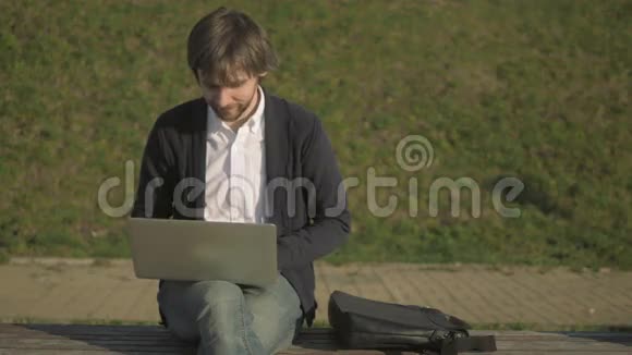 坐在公园长椅上的年轻人在他的笔记本电脑上工作视频的预览图
