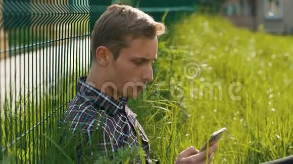 年轻人拿着智能手机坐在草地上视频的预览图