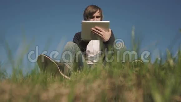 坐在草地上用平板电脑看帅哥的底图视频的预览图