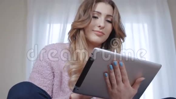 开朗的年轻女性长发坐在床上使用平板电脑视频的预览图