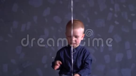 穿着蓝色衣服的滑稽男孩正在灰色的墙上玩红色的气球孩子在家很开心视频的预览图