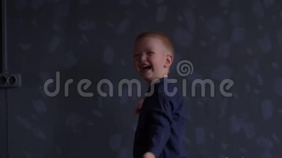 穿着蓝色衣服的滑稽男孩正在灰色的墙上玩红色的气球孩子在家很开心视频的预览图
