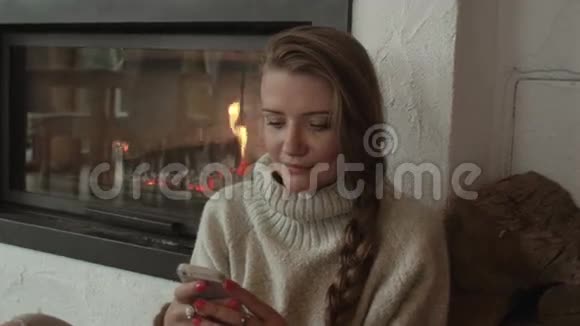 漂亮的女人在家里用手机取暖壁炉视频的预览图