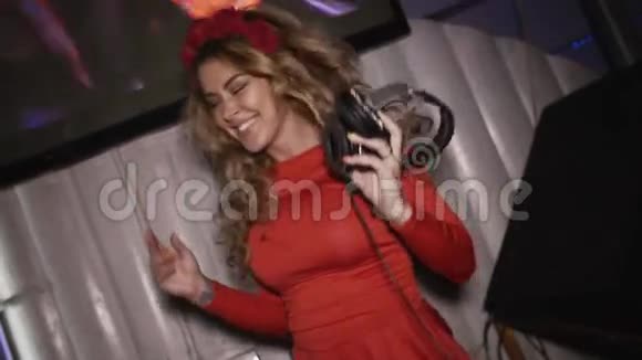 快乐的DJ女孩穿着红色连衣裙头上有轮辋在俱乐部转盘上跳跃乳房视频的预览图
