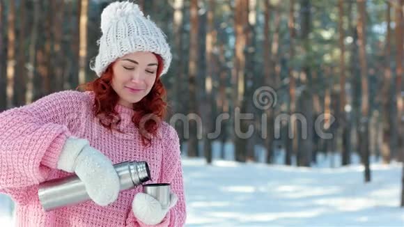 热饮寒冷的冬天女孩从金属热水瓶里倒饮料手里的热水瓶紧紧地拿着手把茶倒进杯子里视频的预览图