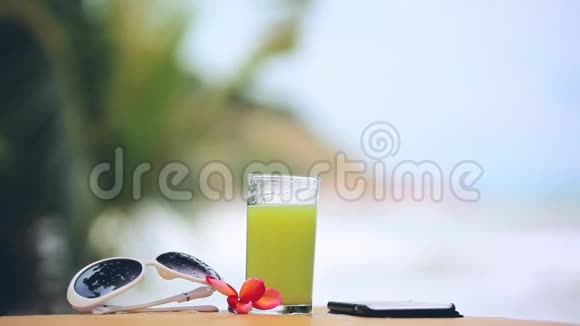 太阳眼镜旁边的一杯猕猴桃汁手机和弗兰吉帕尼花模糊的背景变化焦点视频的预览图