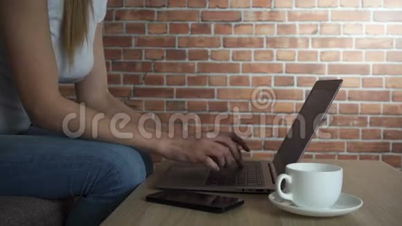 女人在笔记本电脑上打字喝着白色杯子里的咖啡慢动作高清视频视频的预览图