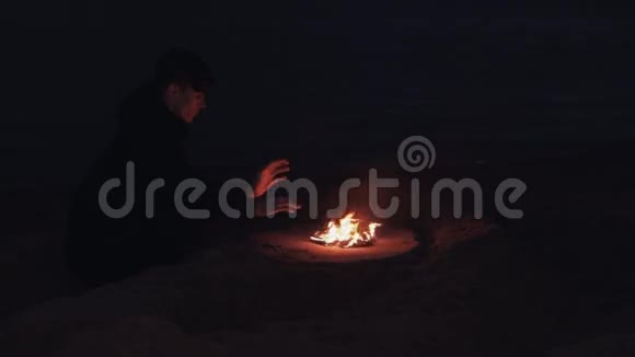无家可归的年轻人坐在海边沙滩上燃烧的鞋子篝火旁视频的预览图