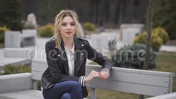 美丽的忧郁的金发女人坐在公园户外的长凳上视频的预览图