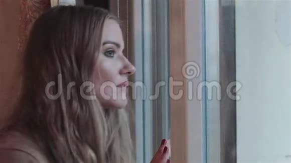 美丽悲伤的年轻女子站在窗边视频的预览图