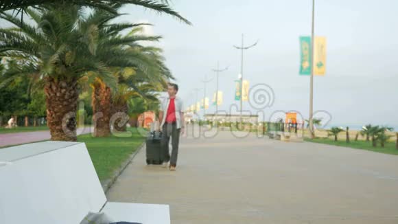 年轻的游客带着一个大手提箱在城市公园周围他停下来环顾四周一个穿白衣服的男人视频的预览图