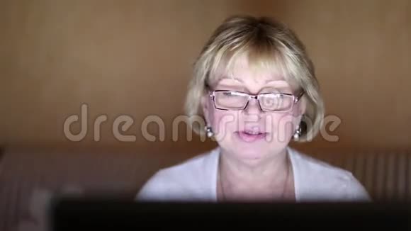 女人坐在黑暗的房间里的沙发上通过笔记本电脑交流视频的预览图