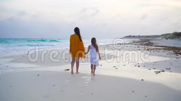 温暖的夜晚热带海滩上的小可爱女孩和年轻母亲视频的预览图