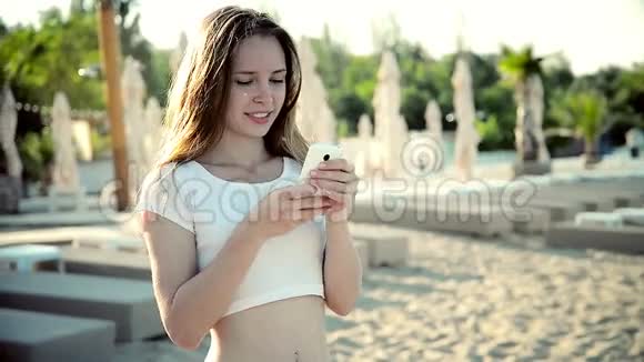 女人在沙滩上用带耳机的智能手机听音乐穿比基尼的女孩视频的预览图