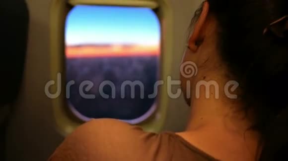 年轻女子在飞机上休息她睡觉透过舷窗观看美丽的日出视频的预览图