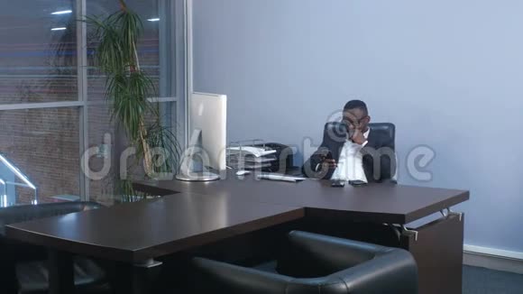 年轻的非洲商人坐在办公室里用智能手机浏览视频的预览图