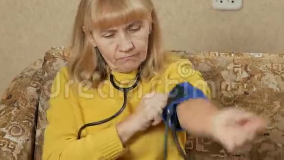 老年妇女在沙发上测量自己家的压力她通过血压计听脉搏视频的预览图