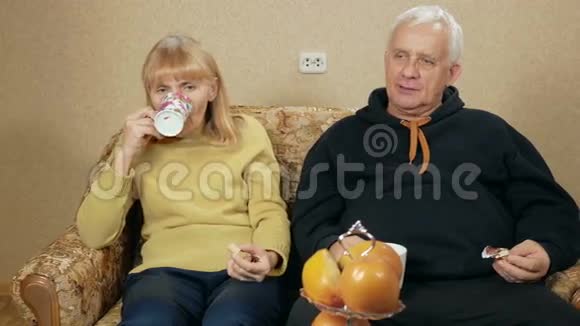 老夫妇喝茶吃糖果夫妻俩坐在家里的沙发上放松假日家庭概念视频的预览图